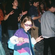 a group of young people standing around each other at a party with one woman wearing sunglasses and the other holding her hand out