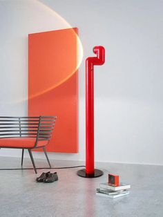 a red lamp is next to a white chair and orange art work on the wall