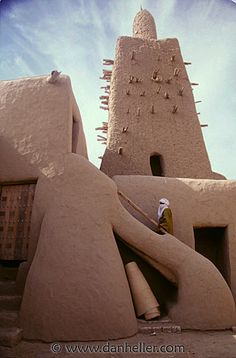 an adobe - style building with two people standing in front of it and another person looking up at the sky