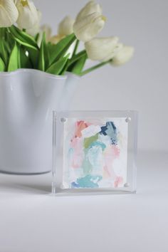 a vase filled with white flowers sitting next to a small glass block on top of a table