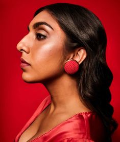 a woman wearing red earrings and a red dress looks off to the side with her head tilted back