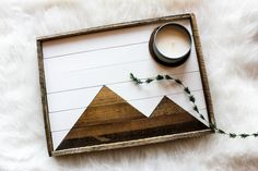 a wooden tray with a candle and some plants on it next to a white rug