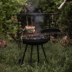 a bbq grill with food cooking on it in the middle of some grass and trees