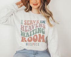 a woman wearing a white sweatshirt with the words i serve in heaven waiting room on it