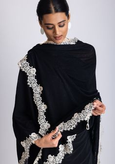 This elegant black knitted cape, crafted from a very soft 100% merino wool, combines warmth and refined designing. The delicate scalloped beige-colored filigree lace border creates a striking contrast against the black wool, adding a touch of sophistication and unique charm. Its soft, free-flowing silhouette makes it a versatile accessory. Whether for daytime outings or evening events, this timeless cape is designed to keep you stylishly cozy while making a bold statement. A must-have piece for Elegant Lace Shawl For Winter, Elegant Winter Lace Shawl, Elegant Cashmere Shawl, Elegant Black Dupatta Shawl, Elegant Merino Wool Shawl For Winter, Elegant Black Lace Shawl, Elegant Lace Shawl Scarf, Knitted Cape, Wool Cape