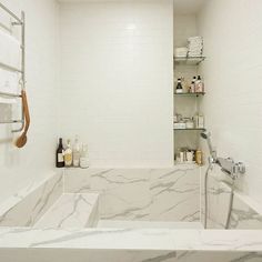 a white bathroom with marble counter tops and shelves above the bathtub is filled with personal care items