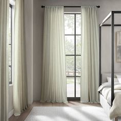 a white bed sitting next to a window in a room with curtains on the windowsill