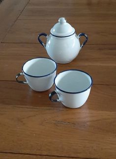 three cups and a teapot sitting on a wooden table