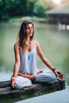 a woman is sitting on a log in the water doing yoga exercises with her eyes closed