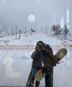 two people standing in front of a window holding snowboards