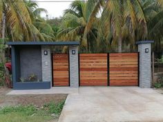 a house with two wooden gates in front of it and palm trees behind the gate