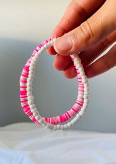 a hand holding a pink and white beaded bracelet on top of a bed next to a wall