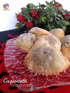 some sugared donuts are on a red plate next to a christmas tree and holly