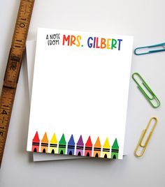 a notepad with crayons on it next to a ruler and paper clips