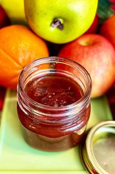 a jar of jam next to some apples and oranges