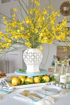 a white vase filled with yellow flowers sitting on top of a table next to plates and silverware