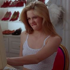 a woman sitting at a desk with a laptop computer in front of her and shoes on the shelves behind her