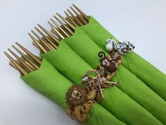 a close up of many different animal decorations on green napkins with gold forks in the background