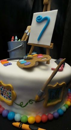 a birthday cake with an easel and paintbrush on it