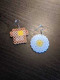 two earrings made out of perfored plastic on top of a wooden table next to each other