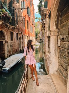 a woman standing on the edge of a bridge next to a boat in a canal