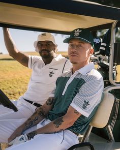 two men sitting in the back of a golf cart, one with tattoos on his arm