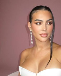 a woman with long hair wearing earrings and a white strapless dress is posing for the camera