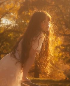 a woman with long hair sitting on top of a wooden bench in the sun light