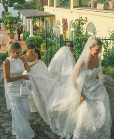 two women in white dresses are walking down the street with veils over their heads