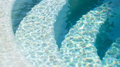 an oval pool with clear blue water and sun reflecting on the surface, as seen from above