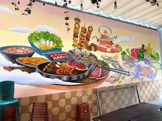 a large mural on the side of a building with food in bowls and pans