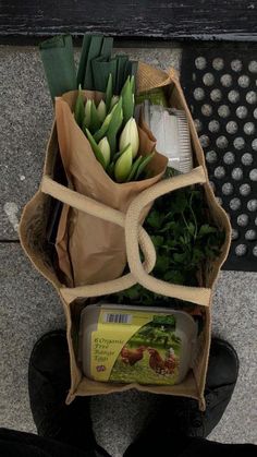 a bunch of flowers sitting in a bag on the ground next to a person's feet