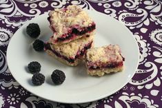 three pieces of cake sitting on top of a white plate with blackberries next to it