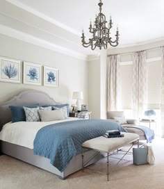 a bedroom with blue and white bedding, chandelier and pictures on the wall