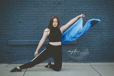 a woman in black is posing with a blue scarf around her neck and arms stretched out