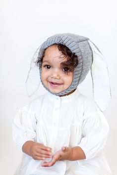 a small child wearing a white shirt and gray hat with ears on it's head