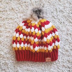 a red, yellow and white knitted hat with a pom - pom