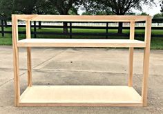 a wooden shelf sitting in the middle of a cement ground next to a fence and trees