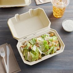 a plastic container filled with salad next to a fork and napkin on top of a wooden table