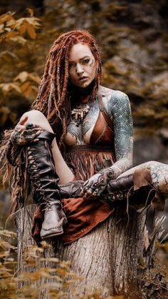 a woman with dreadlocks and tattoos sitting on a tree stump in the woods