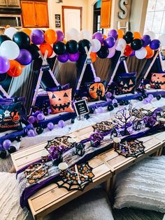 a table topped with lots of halloween decorations and balloons in front of a wall full of pumpkins