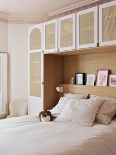 a bed with white sheets and pillows in a bedroom next to a wooden headboard