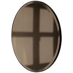 the shadow of a cross is cast on a round wall mirror with black rims