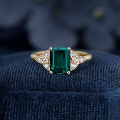 an emerald and diamond ring sitting on top of a blue velvet cushioned surface with white diamonds surrounding it