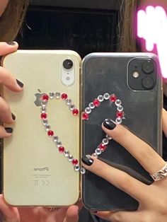 two girls are holding up their cell phones with beads on them and one has a heart