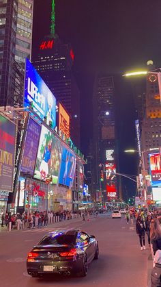 a car driving down a busy city street at night time with billboards on the buildings