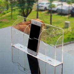 a cell phone is sitting in a clear display case on a table with grass and trees behind it