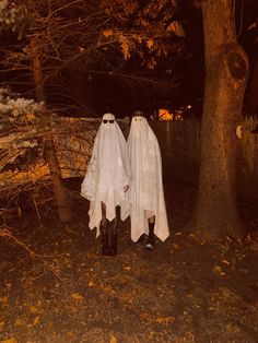 two ghostly people dressed in white standing next to each other under a tree at night