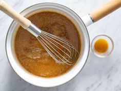 a whisk in a bowl next to an orange liquid and a wooden spoon