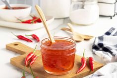 a jar filled with red hot sauce sitting on top of a wooden cutting board next to bowls and spoons